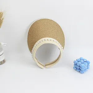 Detail of straw sun visor with pearl trim and headband style on a minimalist white backdrop