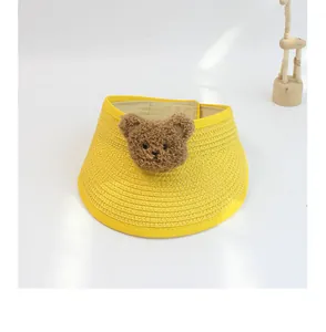 Detailed top view of a yellow woven straw sun hat for kids featuring a cute plush bear decor