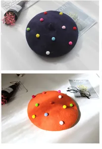 Nahaufnahme von Wollbaskenmützen mit bunten Plüschbommeln in Lila und Orange