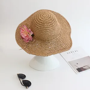 Women's woven sun hat with wide wavy brim and pink floral accent on white background