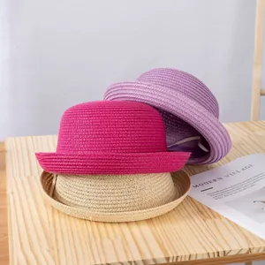 Dettaglio di cappelli di paglia impilati in magenta, viola e crema su un tavolo di legno