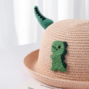 Dettaglio di un cappello di paglia per bambini con design a dinosauro verde e trama intrecciata