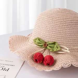 Detail of pink straw sun hat with green bow and red cherry accents for girls