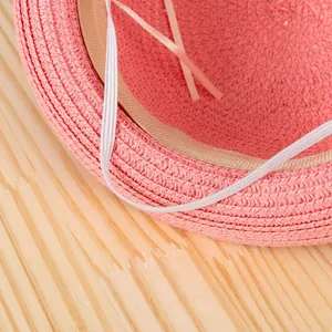 Cappello di paglia rosa con fascia interna e cinturino sottogola elastico su legno