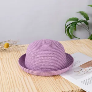 Dettaglio di un cappello di paglia lilla con trama a spirale su un tavolo di legno