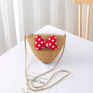 Detail of hand-woven straw crossbody bag featuring a red polka dot bow and metal zipper