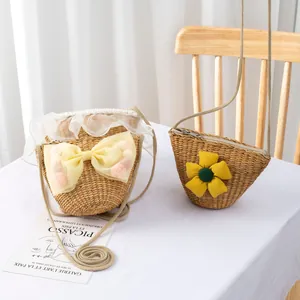 Handmade straw woven bags for kids with mesh bow and floral accents on white table