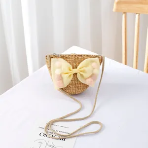 Detail of handmade straw crossbody bag for kids with yellow tulle bow and pom-poms