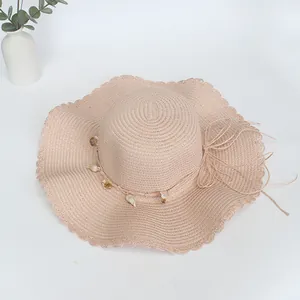 Detail eines beigen Strohhuts mit breiter Krempe, Muscheldekor und gewelltem Spitzenrand