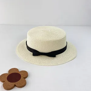 Close-up of a woven cream boater hat with a black bow ribbon on a minimal white background