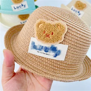 Detail of baby straw sun hat featuring a plush bear patch and breathable woven texture
