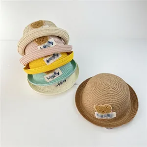 Detail of woven straw sun hats featuring plush bear patches and Lucky labels for kids