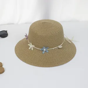 Detail eines Strohhutes mit Spitzenblumen, Perlen und weißem Seil auf dunkelkhaki Geflecht