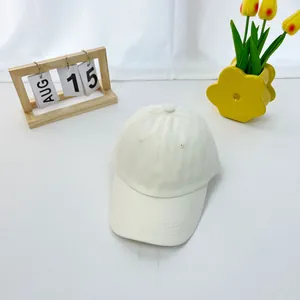 Top view of a minimalist cream cotton baseball cap for kids on a textured white surface