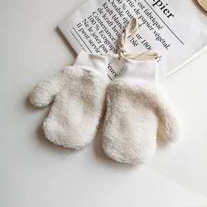 Detail von weichen cremeweißen Lammwoll-Fäustlingen für Kinder mit Strickbündchen und Band