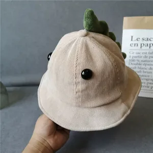 Detailed corduroy texture of beige baby dinosaur bucket hat with green fins