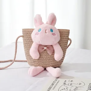 Detail of a girls' straw crossbody bag featuring a pink plush rabbit with blue eyes