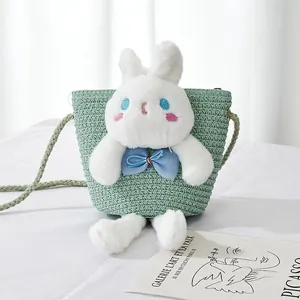 Detail of light green straw crossbody bag featuring a large plush bunny with blue eyes