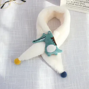 Detail of soft white plush scarf featuring a green cartoon crocodile and colorful pom-poms