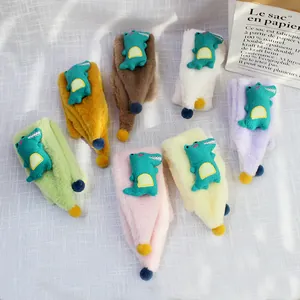 Detail of plush children scarves with cartoon dinosaurs and soft pom-poms in seven colors
