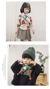 Detail of cute knitted kids scarf featuring green plush dinosaur and soft pom-poms