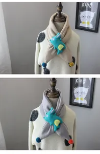 Detail of knit kids scarf with cute green 3D dinosaur plush and colorful pom-poms