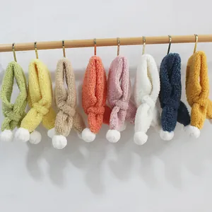 Winter plush scarves for kids with furry balls in multiple colors shown on a wooden rack