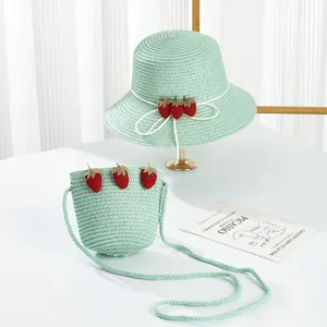 Detail of girls light green straw sun hat and matching crossbody bag with strawberry decor