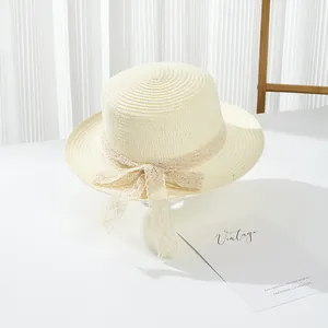 Detailed view of beige flat top straw hat featuring delicate lace bow on white table