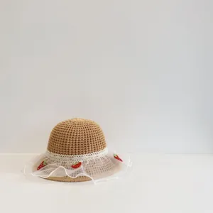 Detail van een strooien zonnehoed voor kinderen met wit kant en schattige aardbeien