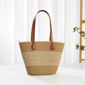 Detail van handgeweven strooien draagtas met beige strepen en bruine leren schouderbanden