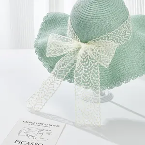 Detailed top view of light green straw sun hat with white lace bow and wavy brim
