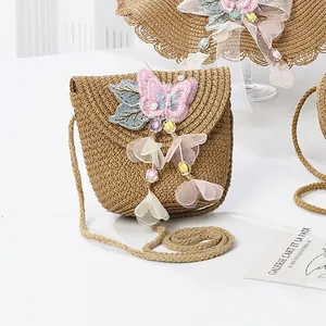 Detail view of woven straw shoulder bag with pink sequined butterfly and floral charms