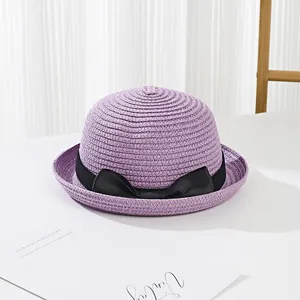 Close-up of lilac straw hat with black bow ribbon on a minimalist white background