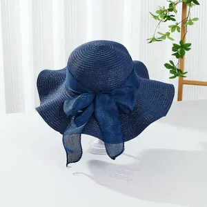 Detail of navy straw sun hat featuring a wavy wide brim and large decorative mesh bow