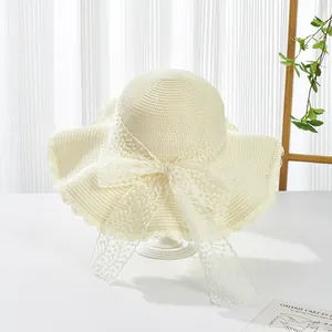 Detailed view of cream straw hat with wide wavy brim and elegant lace bow decoration