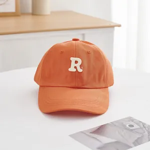 Detailaufnahme der orangefarbenen Baumwollkappe mit hochwertiger weißer R-Stickerei