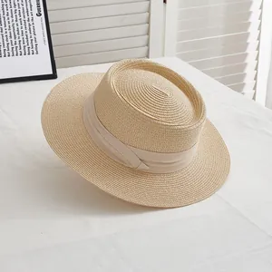 Close-up of beige straw boater hat with ribbon trim on white textured surface