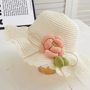 Close-up of beige straw sun hat featuring a large pink fabric flower and lace wavy brim