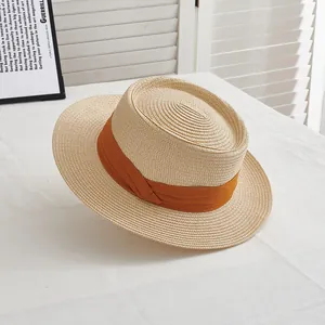 Detail of a natural boater straw hat with wide orange ribbon on a clean white table