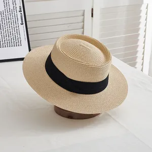 Detail of a beige flat-top straw hat with a wide black ribbon and fine woven texture