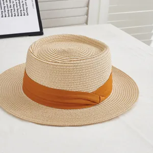 Detail of light beige straw boater hat featuring a vibrant orange decorative ribbon band