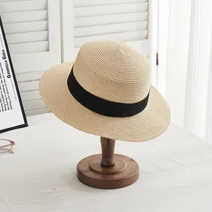 Close-up of beige boater straw hat with black ribbon on wooden stand with home decor