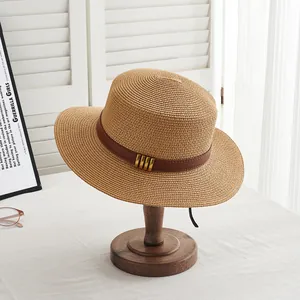 Détail du chapeau de paille d'été avec ruban en cuir brun et boucles métalliques dorées