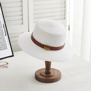 Détail d'un chapeau de paille blanc avec bande en cuir marron et boucles en métal doré