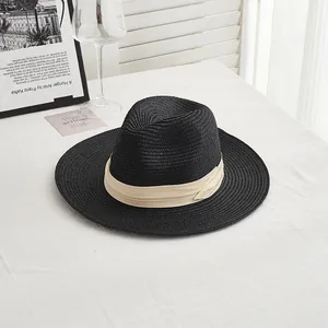 Detail of classic black straw fedora featuring a beige ribbon bow on a white table