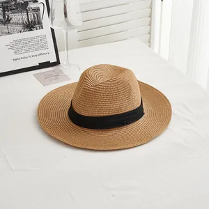 Detail of a brown woven straw fedora hat with a black satin ribbon on a white table