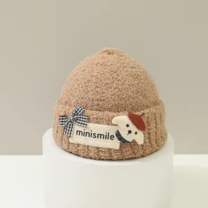 Dettaglio del cappello in maglia marrone per neonati con toppa a cucciolo e fiocco a scacchi