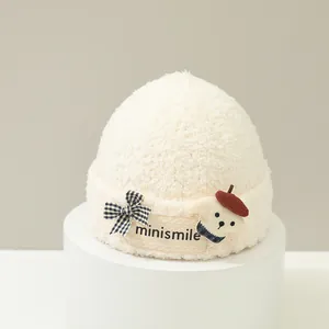 Dettaglio del cappello di peluche bianco con toppa a orsetto e fiocco a quadretti