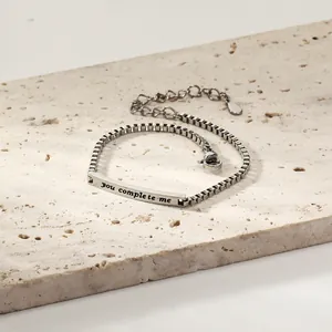 Détail macro du bracelet à chaîne gourmette avec barre gravée 'you complete me'